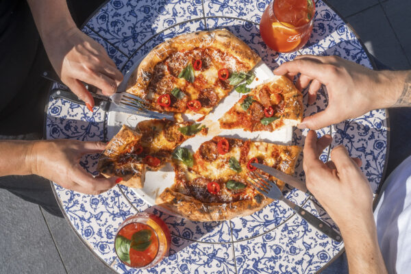 hands grabbing slices of pizza on a blue and white sunlit table