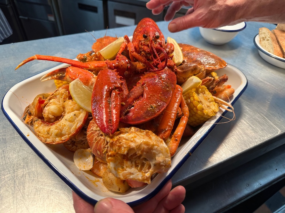 Lobster on top of a pile of seafood on a white rectangular dish with a blue rim